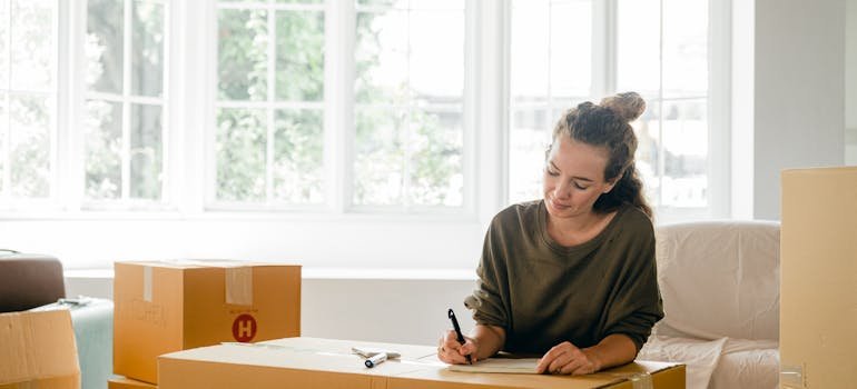 Tips For Moving A Grand Piano In Cincinnati 3 A woman surrounded with cardboard boxes is writing a checklist.
