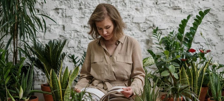 Tips For Moving With Plants Long-Distance 1 Person reading a guide on preparing houseplants for moving, surrounded by potted plants.