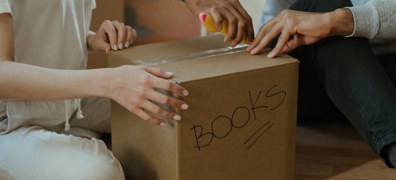 How To Unpack After Moving To Milford Ohio 2 a couple unpacking a box labeled BOOKS, showing how to unpack after moving