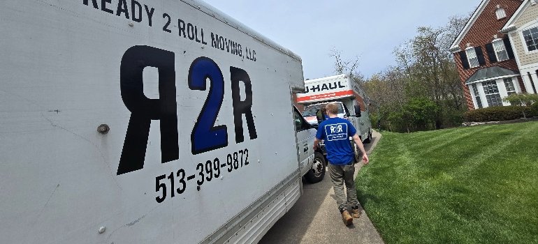 Packing Service 4 A moving truck with the logo "R2R" and a worker in a blue shirt walking towards a U-Haul truck in a residential area.