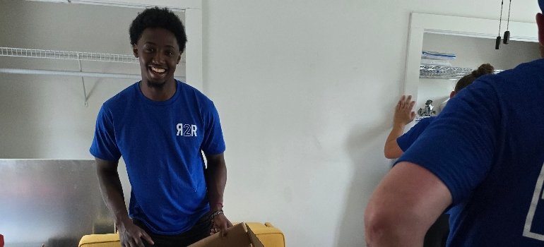 Local Movers 4 A person in a blue shirt is unpacking a cardboard box in a room with white walls and a closet shelf.