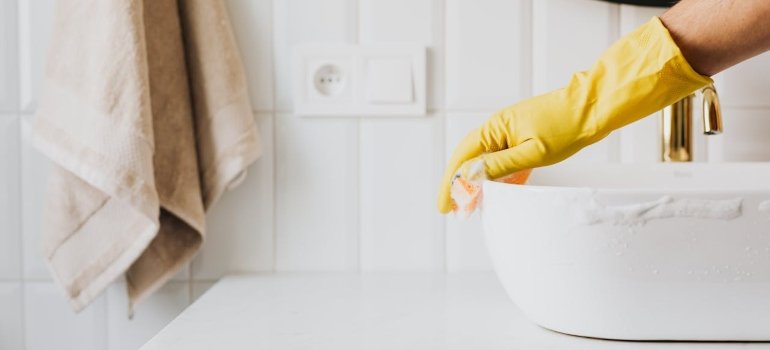 How To Clean An Apartment Before Moving In 1 A hand in a yellow glove scrubs a white bowl in a bathroom