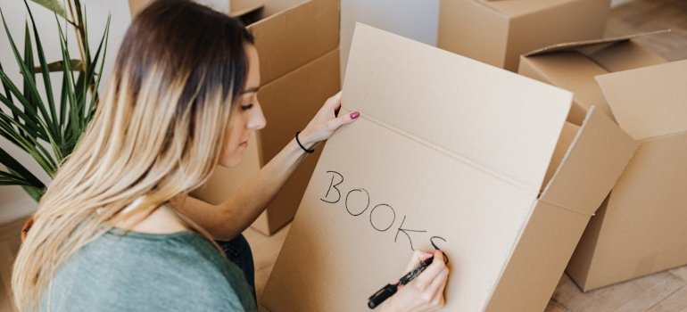 The Best Way to Pack Books for Moving 3 A person labels a cardboard box with the word "BOOKS," knowing how to pack books for moving