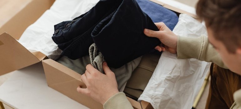 How to Pack Clothes for Moving Like a Pro 4 Person unpacking a labeled wardrobe box, showing the best way to move clothes and keep them organized.