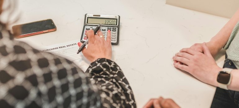 Moving Estimate vs Final Invoice: What’s the Difference 1 Close-up of two people using a calculator and reviewing documents, showing how movers and clients finalize charges and understand the difference between a moving estimate vs final invoice.