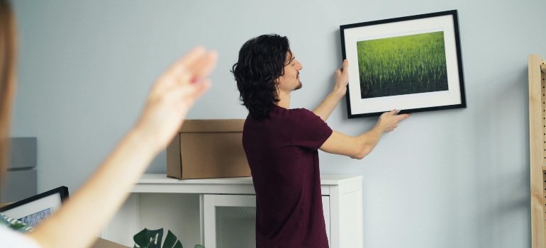 Practical Checklist of Things You Need When Moving Out 2 Man hanging a framed picture on the wall while unpacking Things You Need When Moving Out.