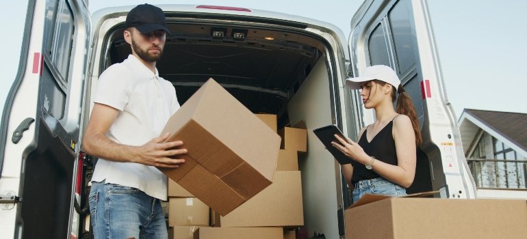 Moving Estimate vs Final Invoice: What’s the Difference 3 Two movers unloading cardboard boxes from a van while one uses a tablet to check inventory during a relocation.