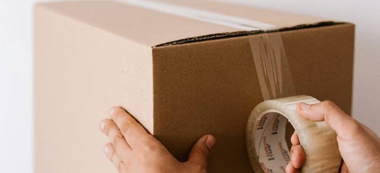 Packing supplies you should never skip for a long distance move 2 Hands taping box using packing supplies you should never skip